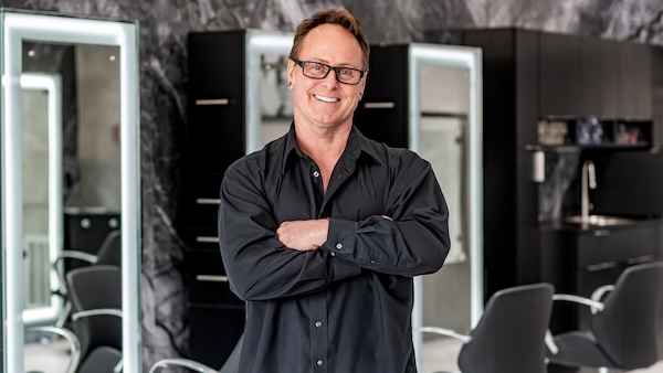 Jay our hairstylist posing for the camera wearing eyeglasses and smiling